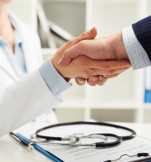 A doctor and patient shaking hands over papers.