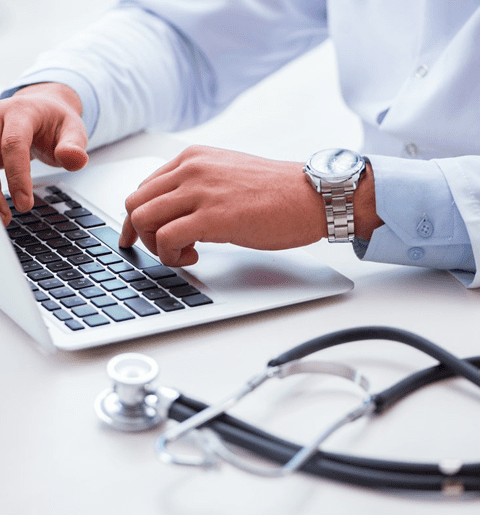 A doctor is using his laptop while sitting at the desk.